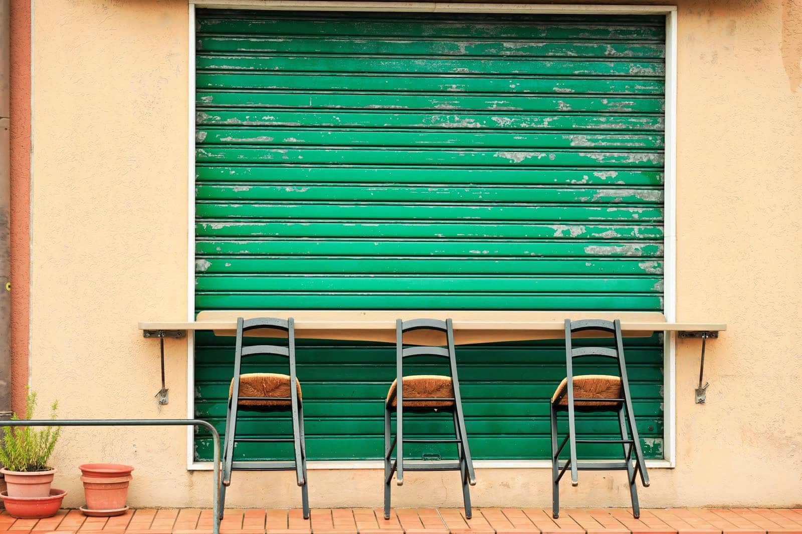 Persiana metálica verde con la pintura levantada y el metal a la vista