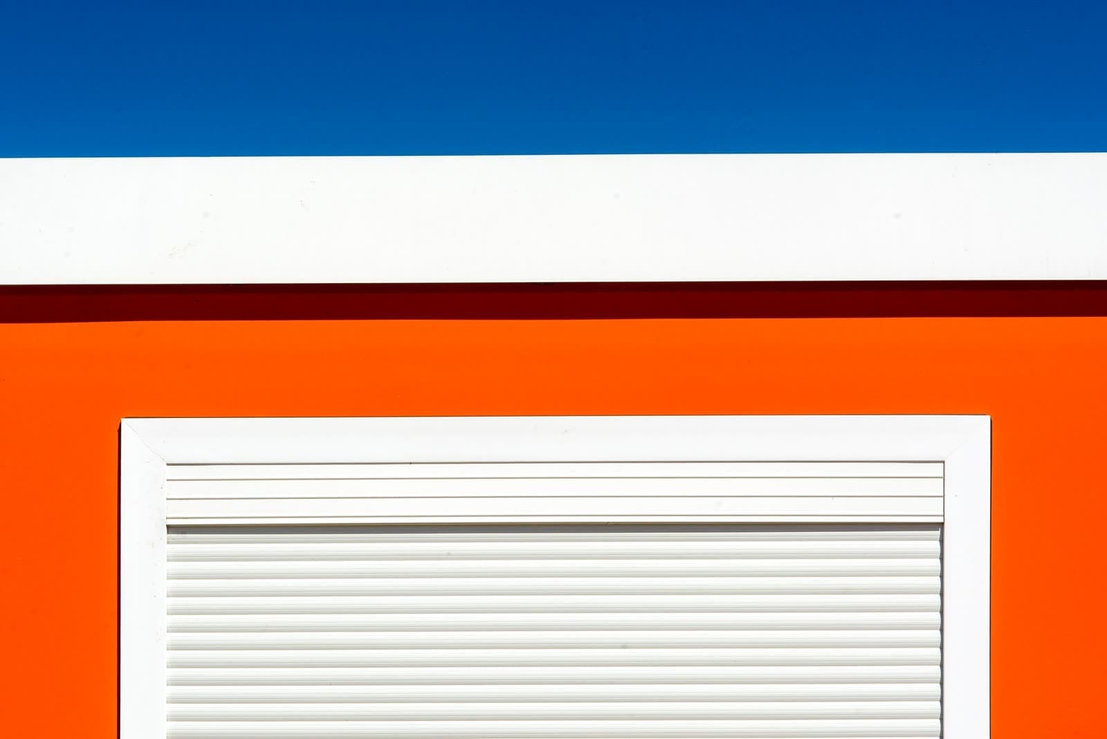 Persiana enrollable blanca con el cajón visible sobre una pared naranja