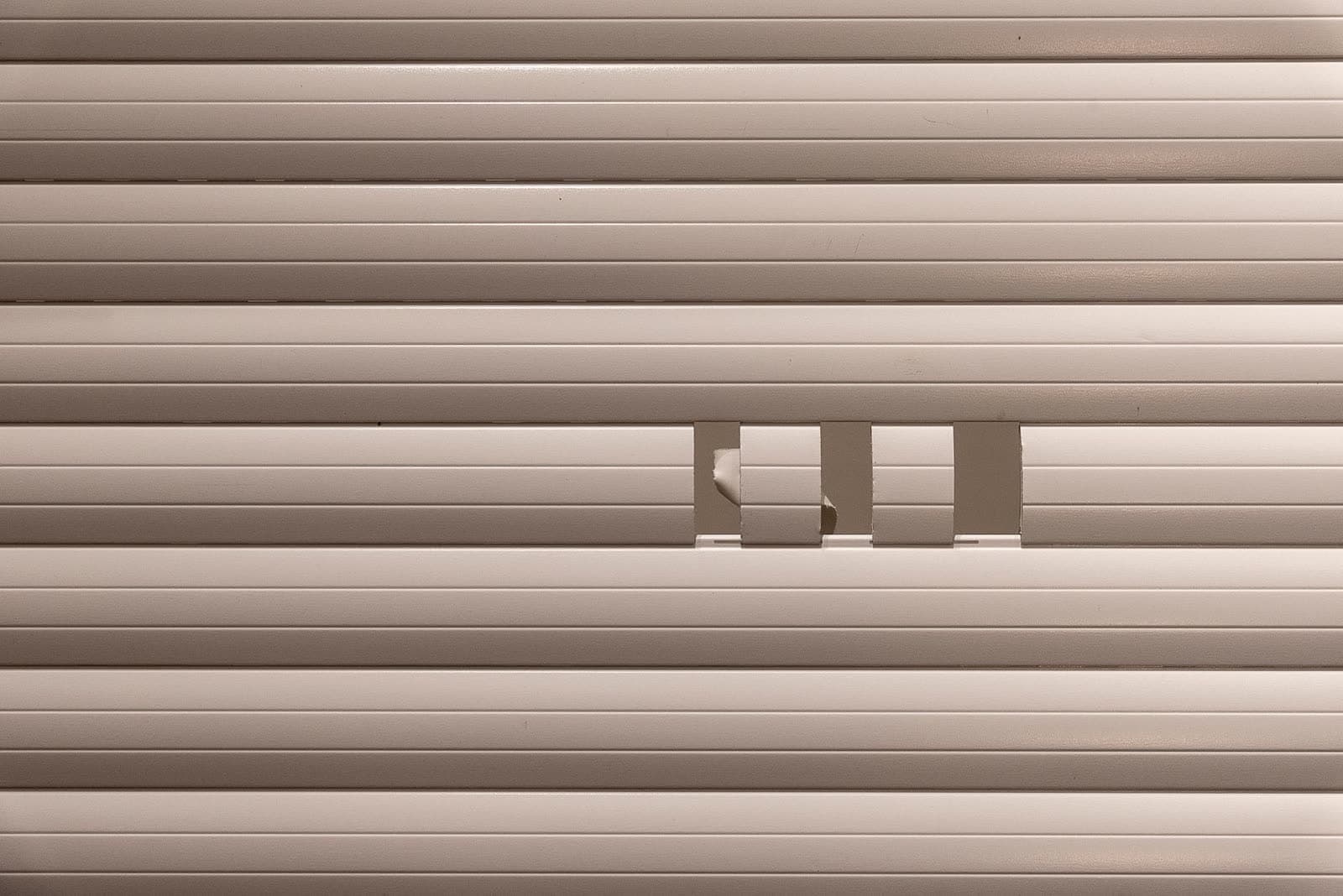 Primer plano de un paño de persiana beige con los recortes de ventilación de una lama abiertos