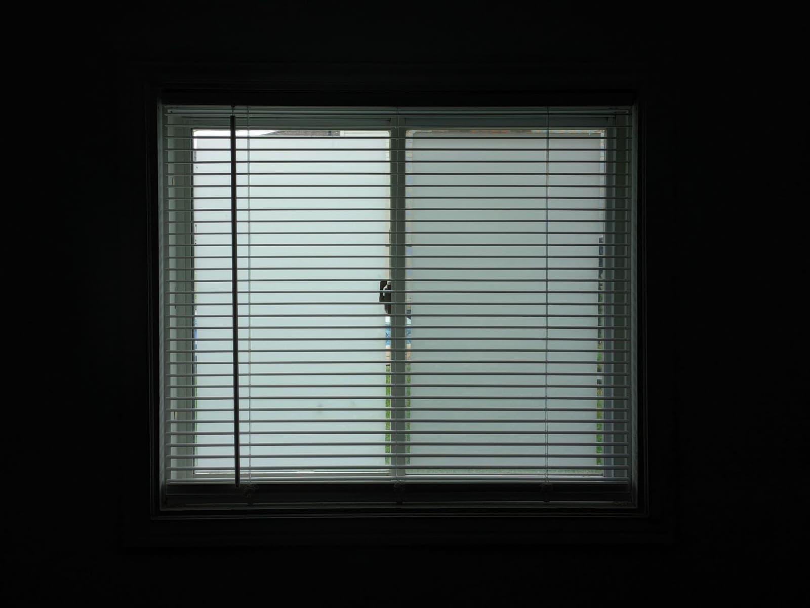 Ventana con la persiana veneciana bajada, vista desde una habitación a oscuras